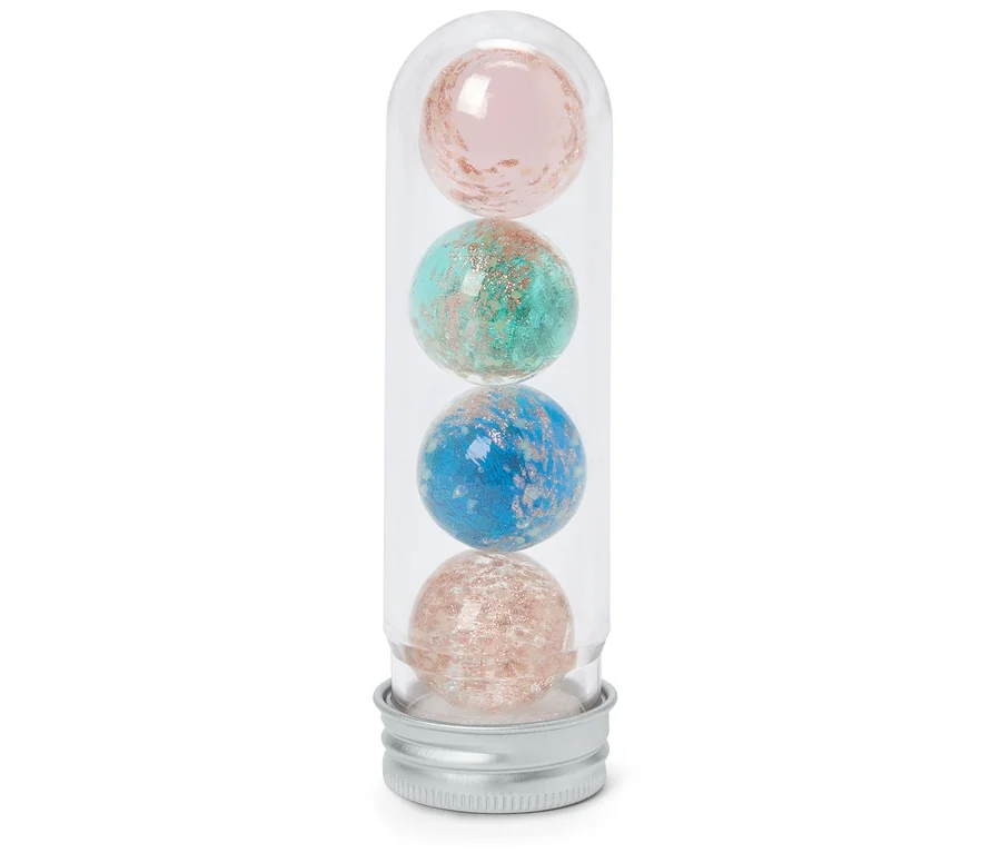 Quatre bombes de bain scintillantes roses, turquoise, bleues et or rose sont empilées dans un tube transparent avec un bouchon argenté.