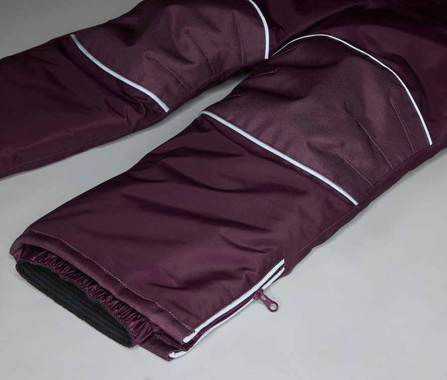 Gros plan sur un pantalon aubergine avec des détails blancs et une fermeture éclair en bas de la jambe.