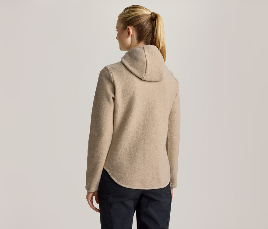 Femme vue de dos, portant une veste polaire à capuche beige et un pantalon foncé. Ses cheveux blonds sont attachés en queue de cheval.