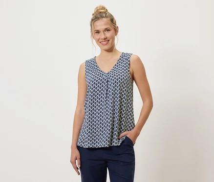 Une femme portant un chignon porte un haut à motifs bleu et blanc et un pantalon bleu, une main dans la poche.