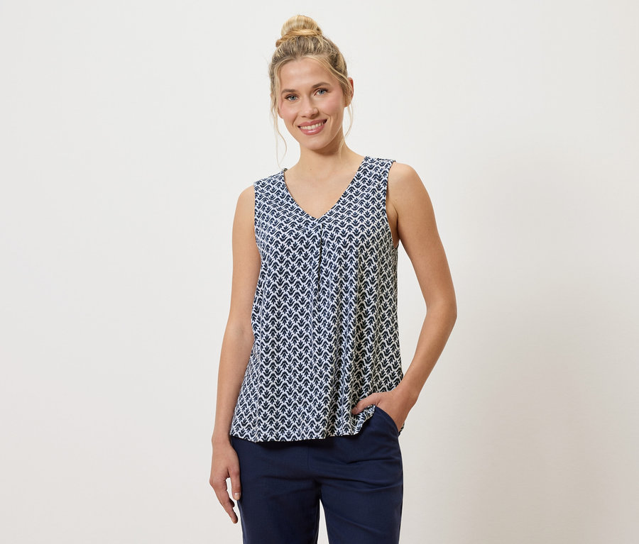 Une femme portant un chignon porte un haut à motifs bleu et blanc et un pantalon bleu, une main dans la poche.