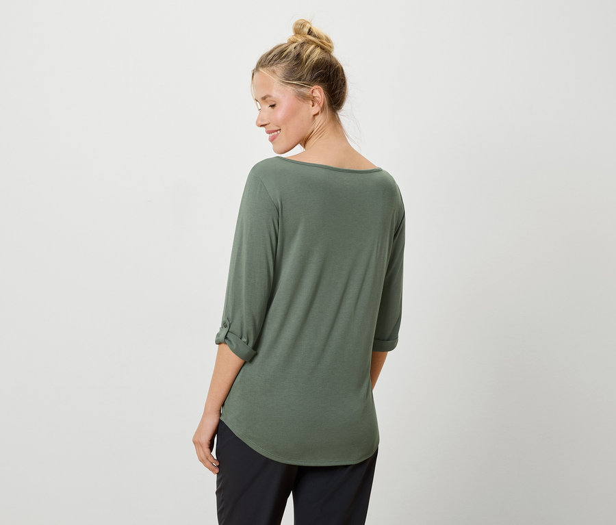 Une femme portant un chignon porte un haut vert et un pantalon noir.