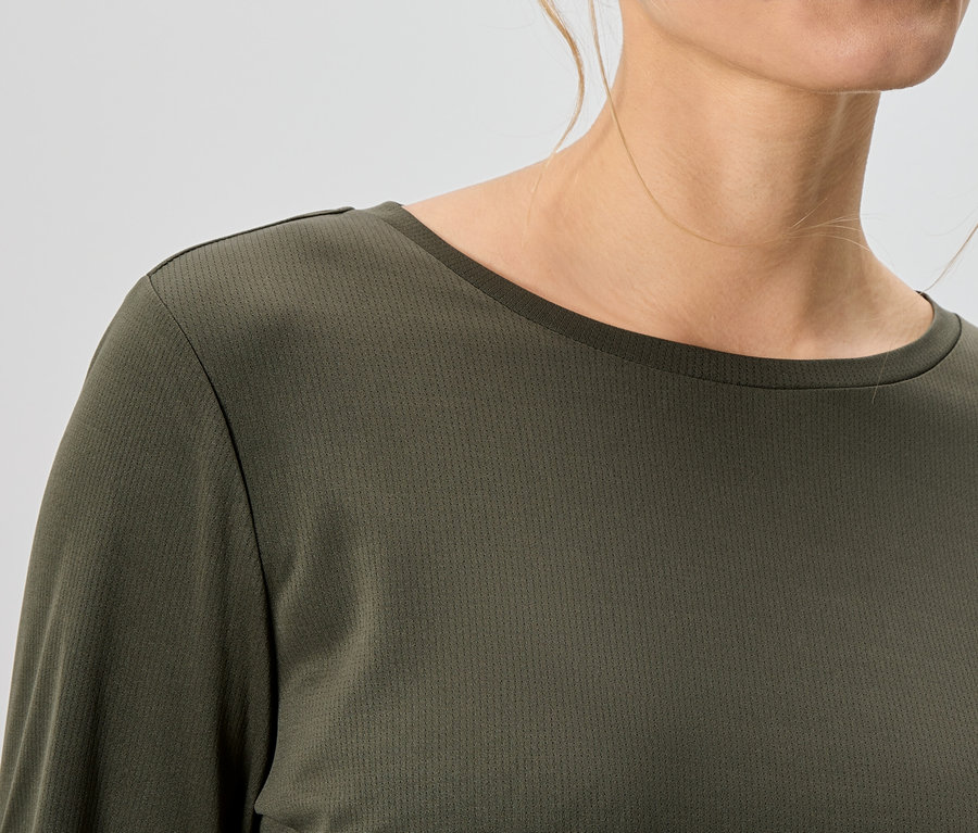 Gros plan d'une femme portant un haut olive à manches longues.
