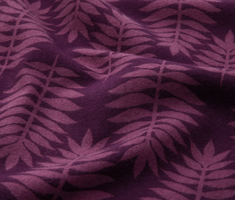 Gros plan d'un tissu couleur prune avec un motif répétitif de feuilles de fougère violet foncé, présentant de doux plis.