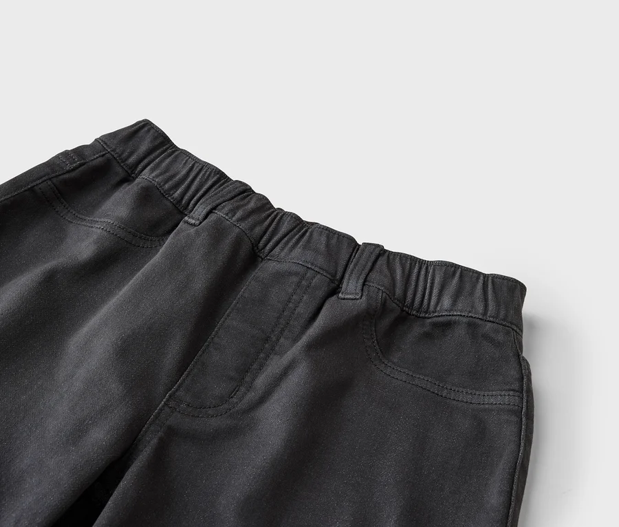 Gros plan du haut d'un pantalon noir avec une taille élastique, des passants de ceinture et des poches avant avec des coutures visibles.