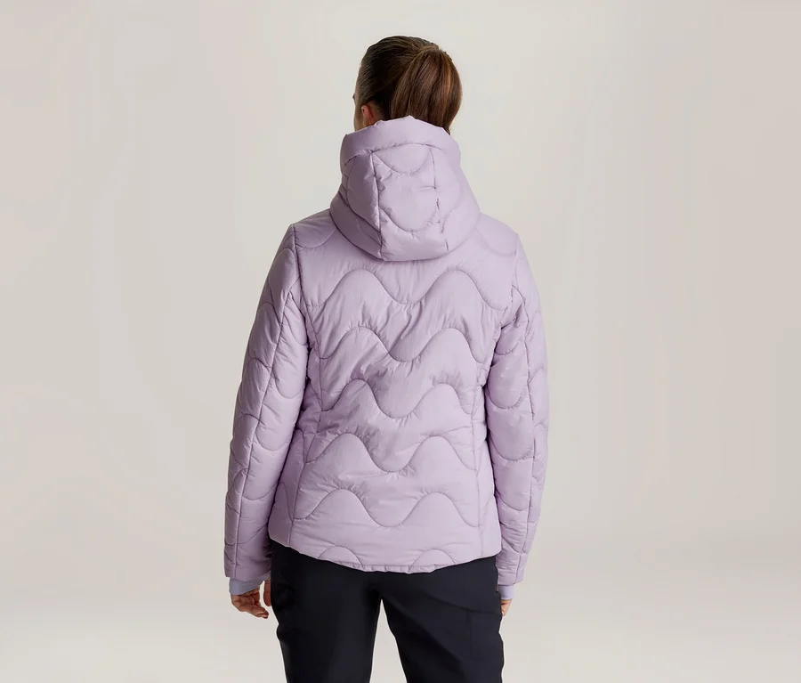 Femme de dos portant une veste matelassée violet clair à capuche avec un motif ondulé, et un pantalon noir.