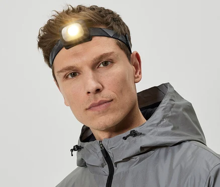 Un homme portant une lampe frontale et une veste à capuche grise.
