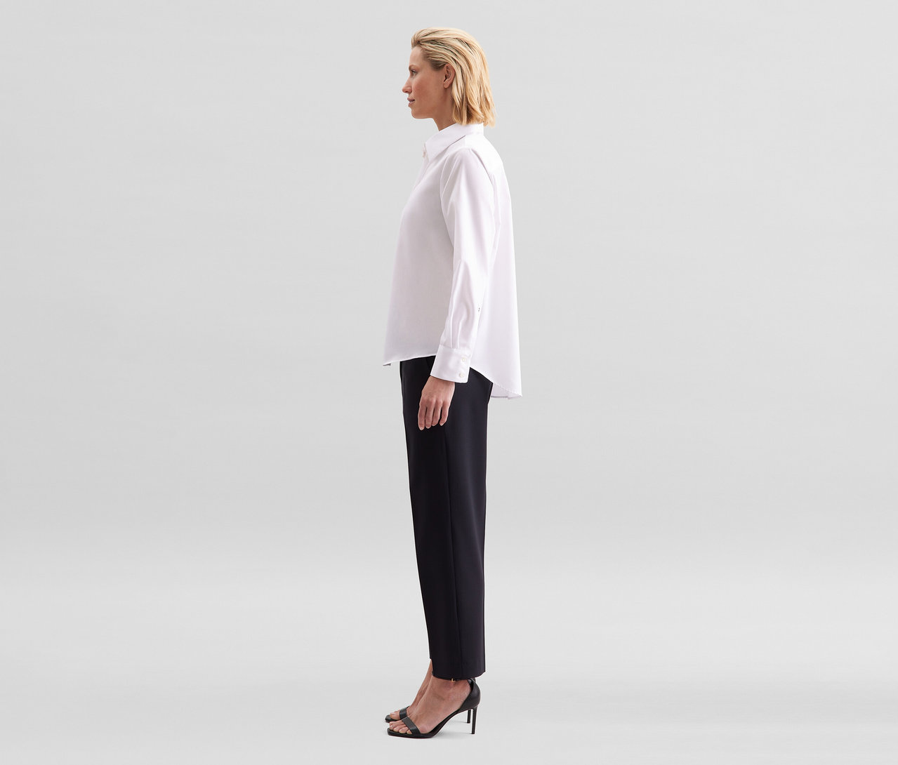 Une femme de profil porte un chemisier sans repassage Seidensticker blanc et un pantalon noir.