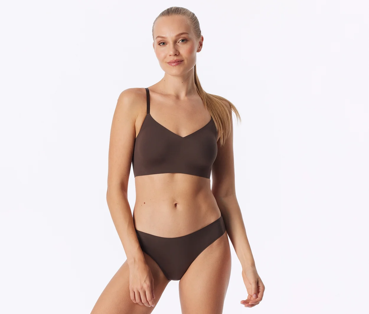 Jeune femme aux cheveux blonds attachés, debout et regardant l'appareil photo, portant un soutien-gorge marron et une culotte assortie.