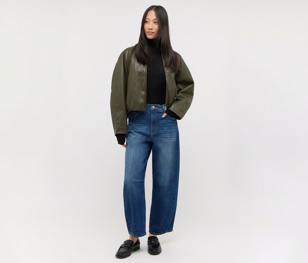 Femme en col roulé noir, veste bomber vert foncé, jean large et mocassins noirs.