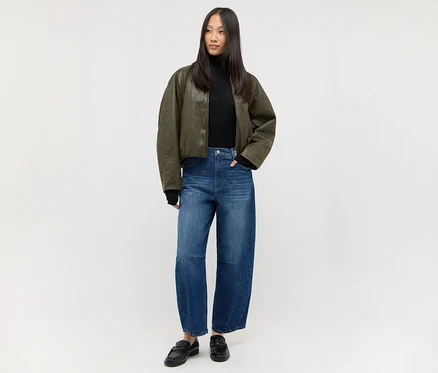 Femme en col roulé noir, veste bomber vert foncé, jean large et mocassins noirs.