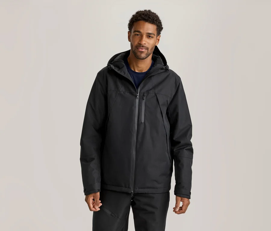 Homme portant une veste noire à capuche, un t-shirt bleu foncé et un pantalon noir.