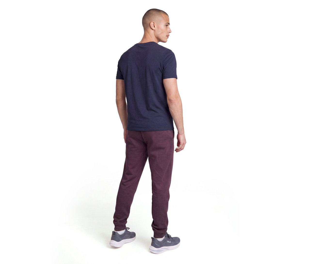 Un homme vu de dos, portant un t-shirt bleu marine, un pantalon de survêtement bordeaux et des baskets grises. Il regarde par-dessus son épaule droite.