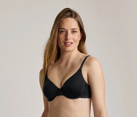 Une femme aux longs cheveux ondulés châtain clair porte un soutien-gorge noir à armatures avec des finitions en dentelle.