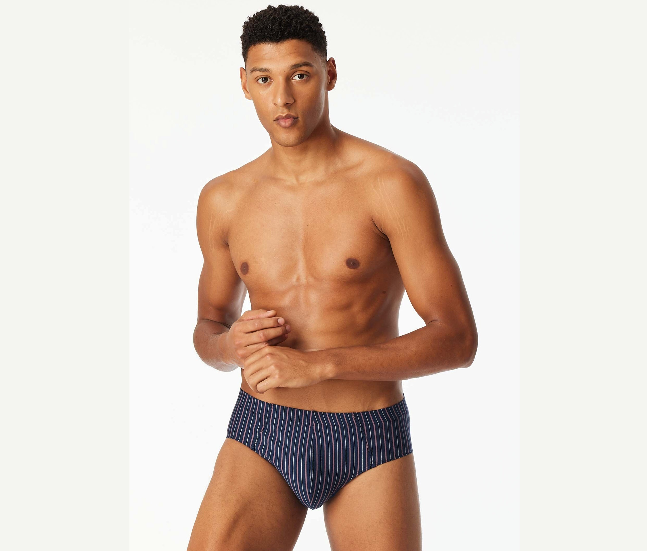 Un homme torse nu pose en slip bleu rayé.