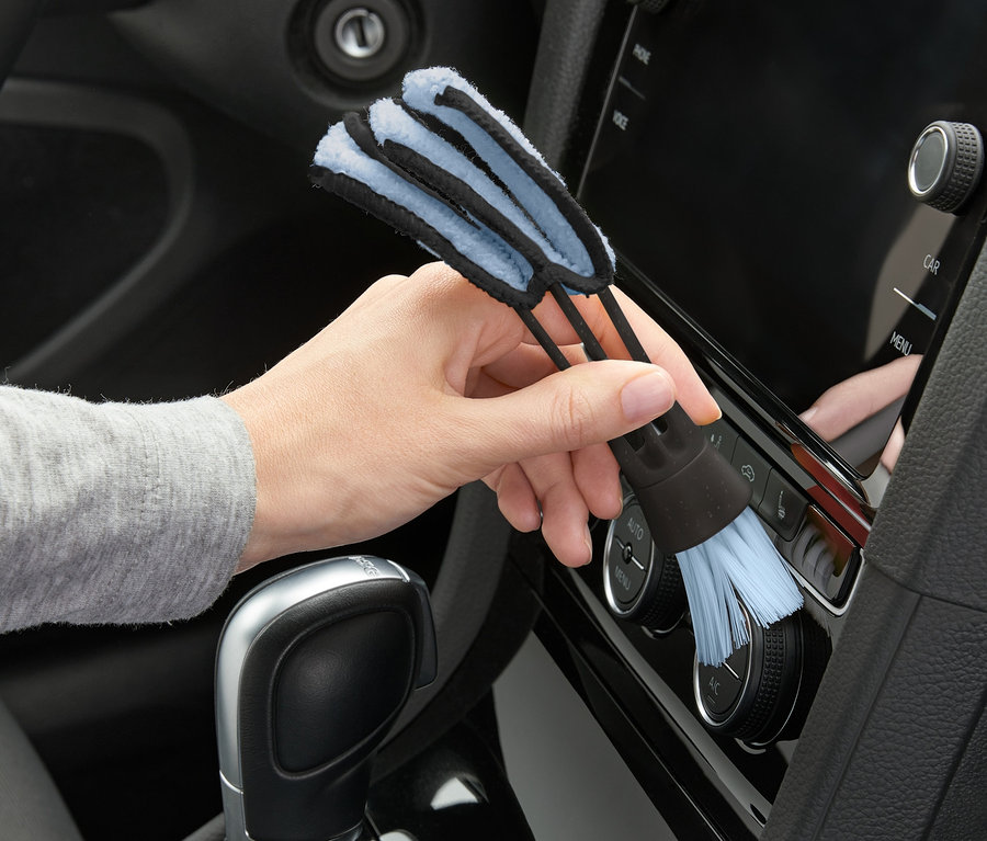 Une main utilise une brosse de nettoyage 2 en 1 pour nettoyer le tableau de bord d'une voiture.