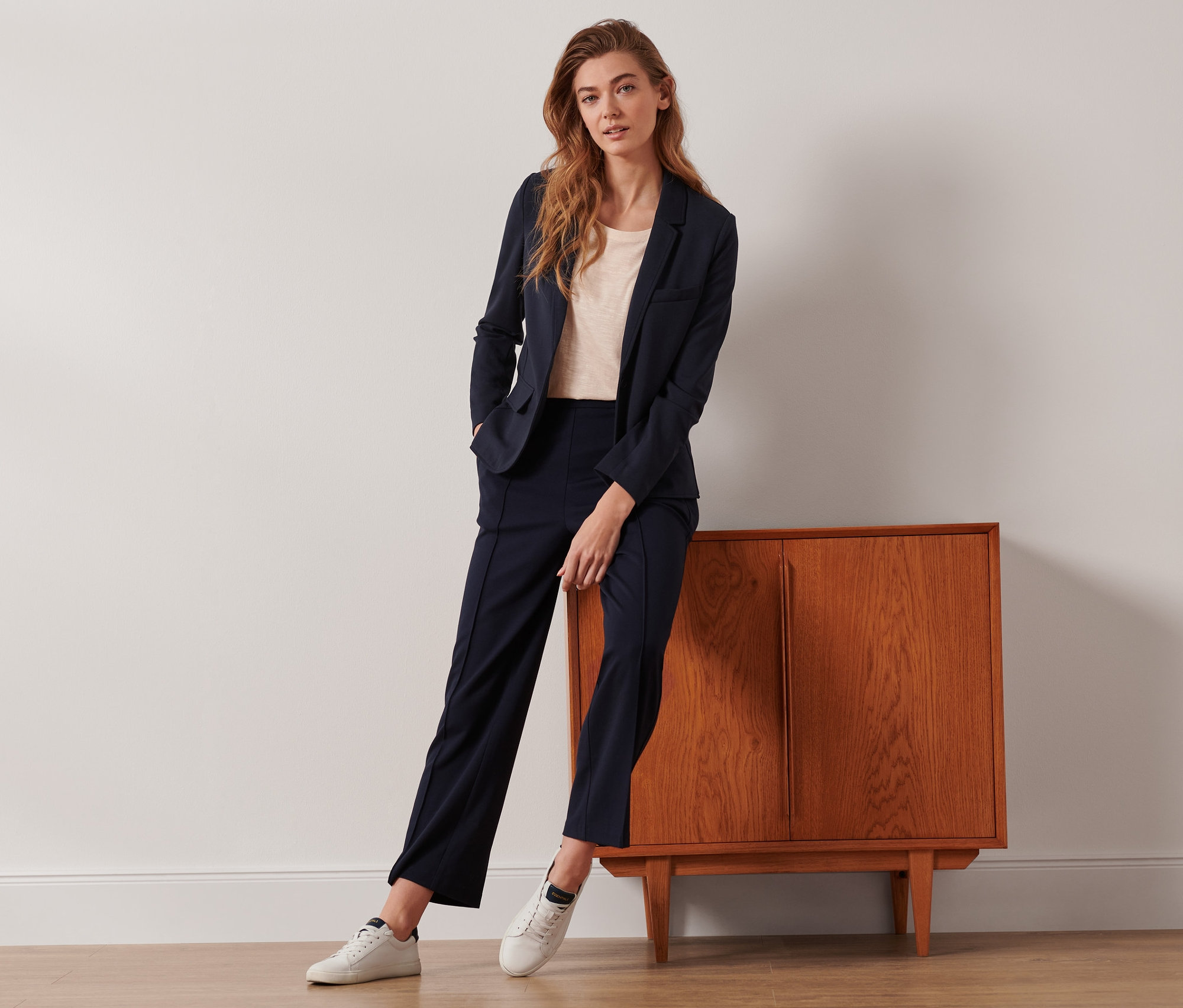 Une femme pose, adossée à une armoire, portant un blazer en jersey et un pantalon en jersey bleu foncé avec nervure.