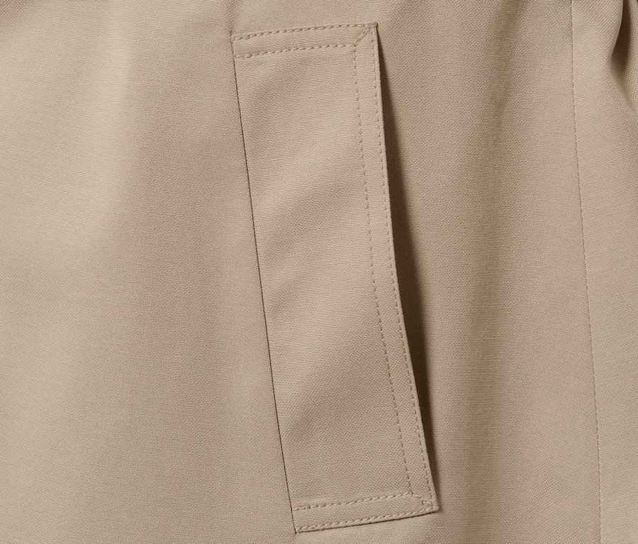 Gros plan sur un trench-coat beige avec une poche.