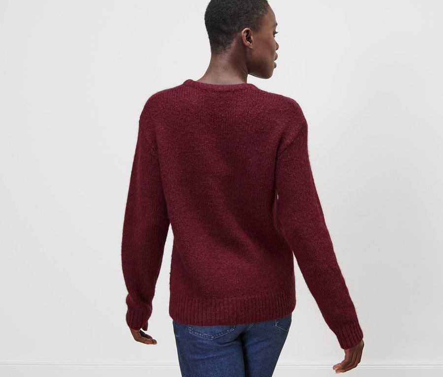 Une femme porte un pull en grosse maille avec de la laine, rouge bordeaux et un jean.