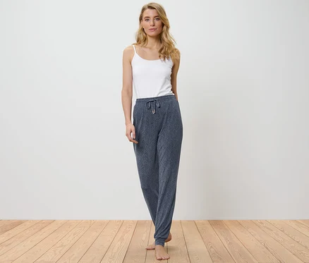 Une femme porte un pantalon de pyjama et un débardeur blanc.