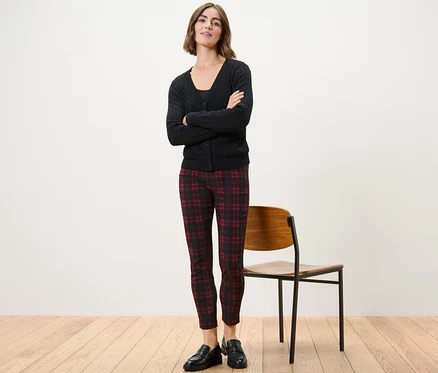 Une femme se tient debout, les bras croisés, portant un pantalon stretch à carreaux, une veste noire et des chaussures noires.
