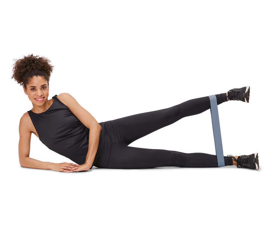 Une femme est allongée sur le côté et fait de l'exercice avec 3 bandes d’entraînement autour de ses jambes.