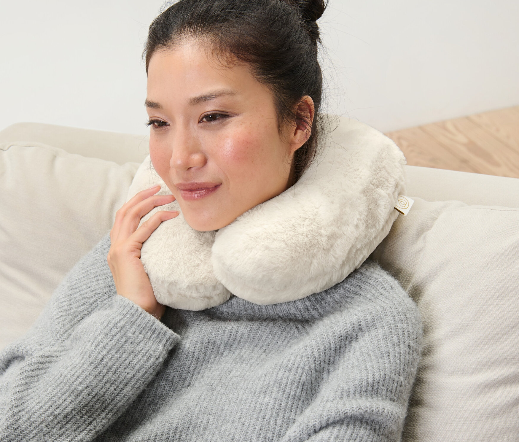 Femme assise sur un canapé avec un coussin de nuque en mousse à mémoire de forme.