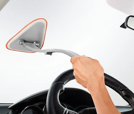 Une main tient un outil de nettoyage pour vitres intérieures de voiture et nettoie le pare-brise d'une voiture.