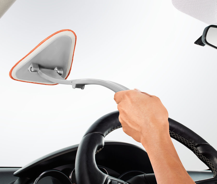 Une main tient un outil de nettoyage pour vitres intérieures de voiture et nettoie le pare-brise d'une voiture.