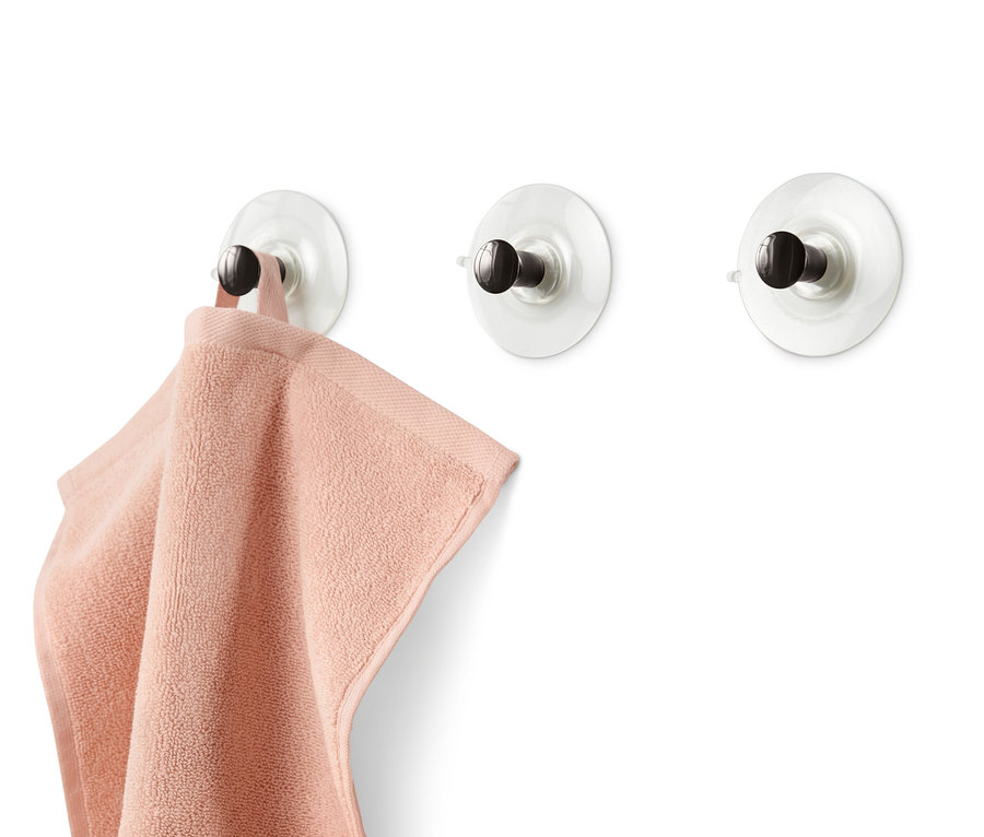 Trois crochets à ventouse sont fixés sur un mur blanc, une serviette rose est suspendue à l'un d'eux.