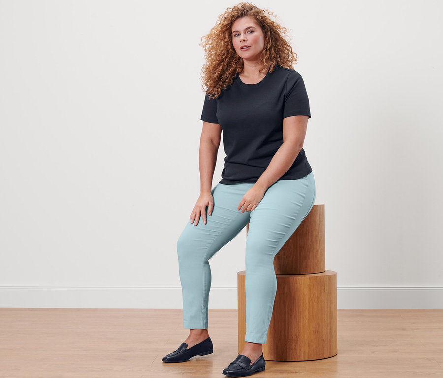 Femme assise sur des marches en bois portant un t-shirt basique bleu foncé et un pantalon stretch.