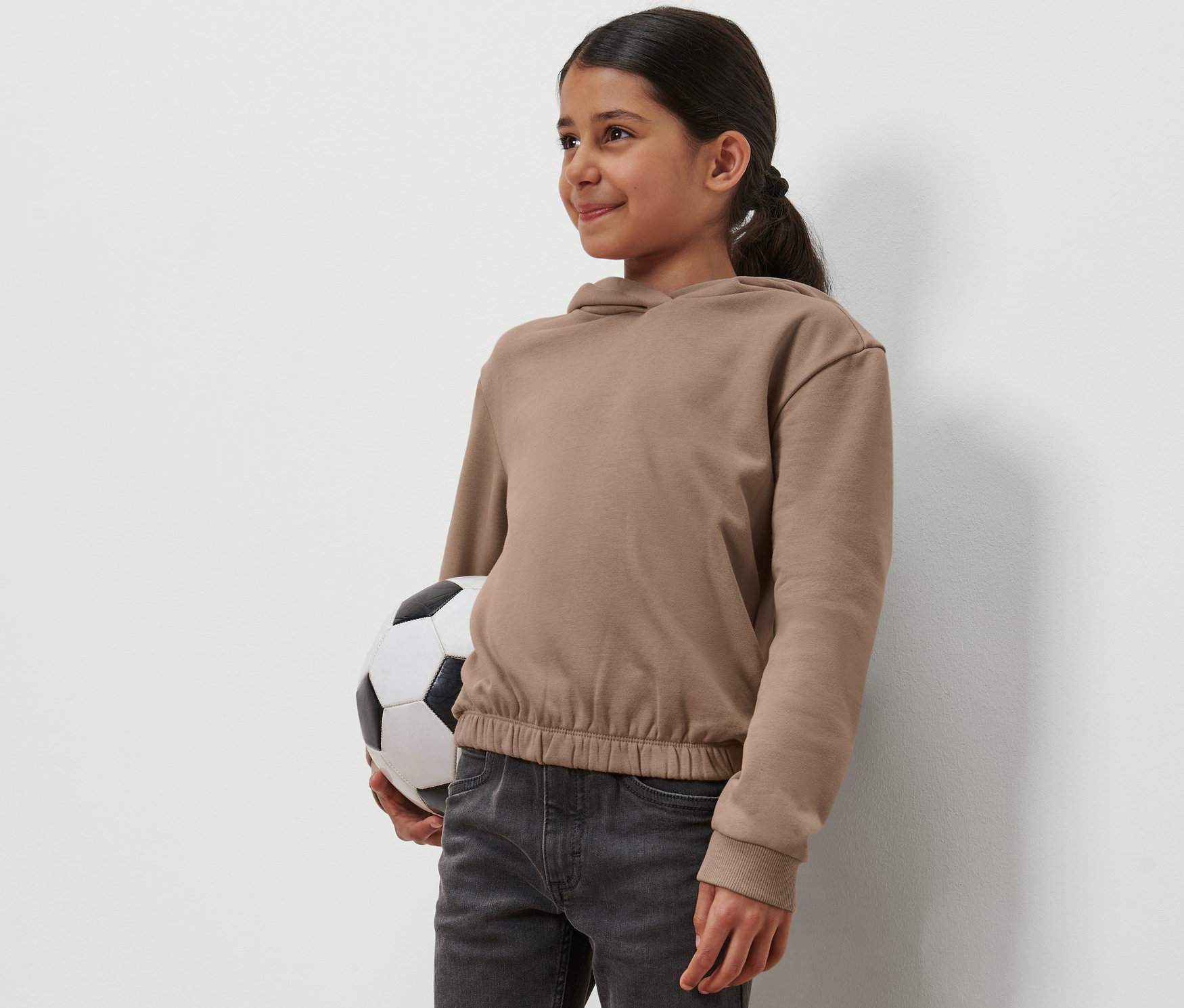 Une fille tient un ballon de foot et porte un sweat-shirt à capuche pour enfants.