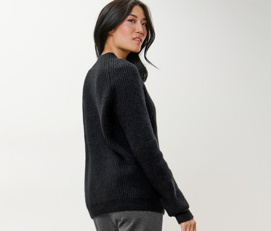 Femme regardant par-dessus son épaule portant un pull noir à col droit en grosse maille.