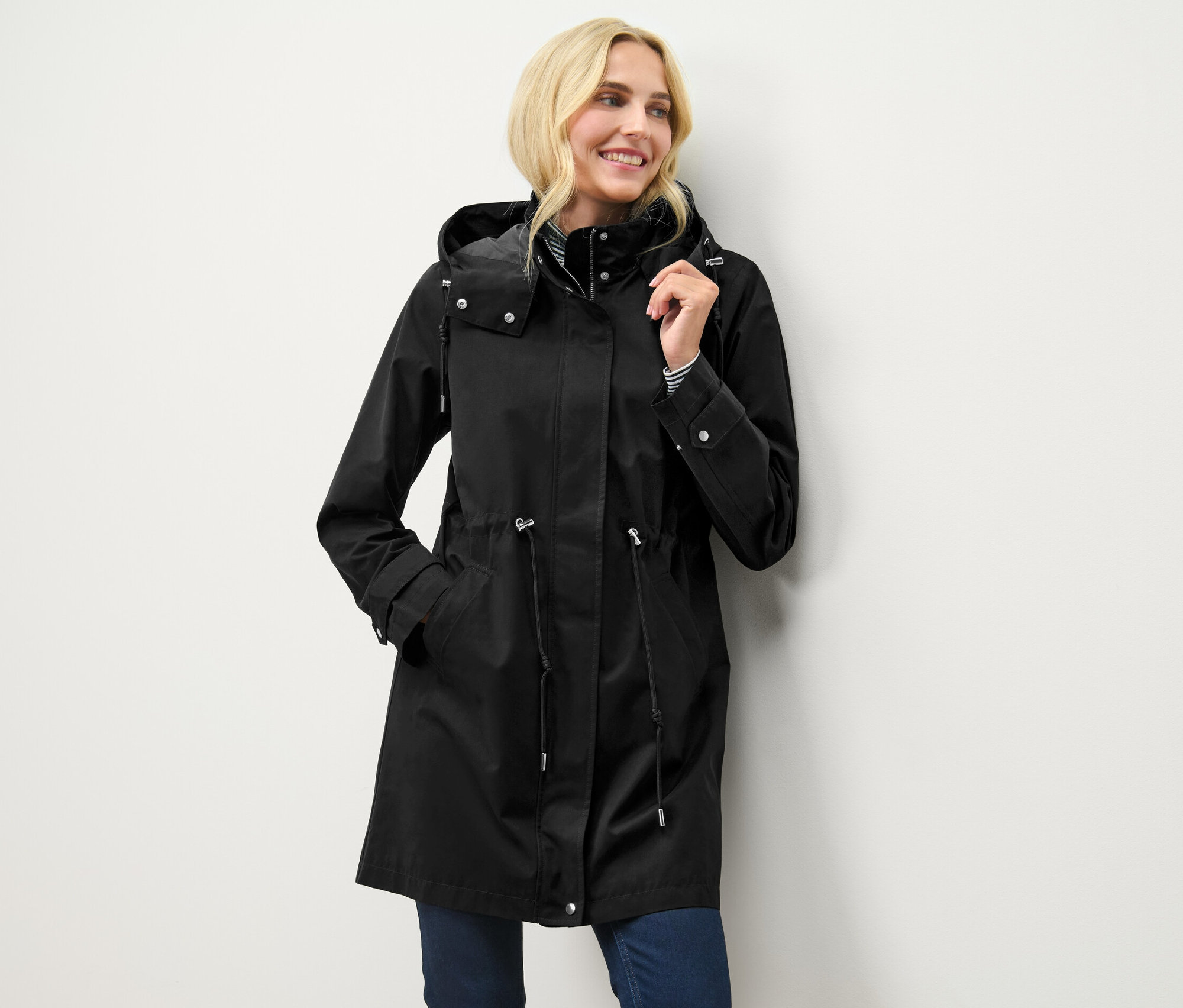 Femme blonde posant dans une parka noire à capuche.