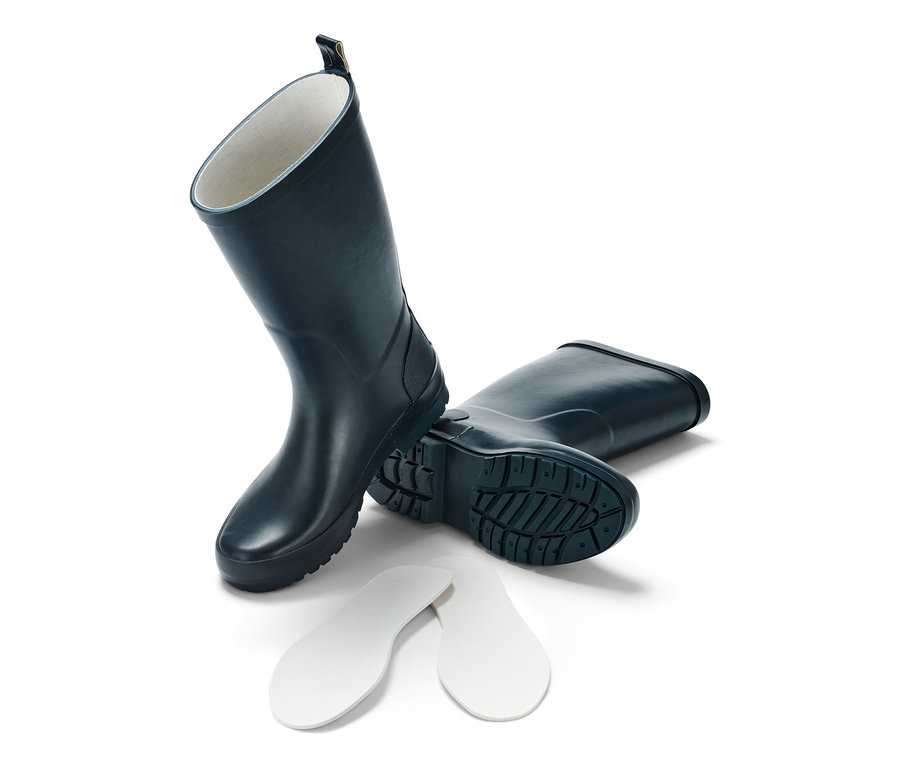 Bottes de pluie bleues pour enfants, une debout, l'autre couchée, avec des semelles à côté.