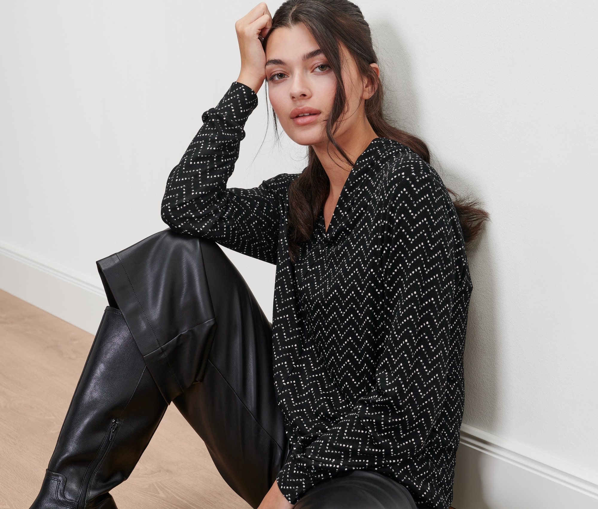 Une femme est assise par terre et porte un pantalon en cuir noir et un t-shirt manches longues avec encolure en V, imprimé intégral.
