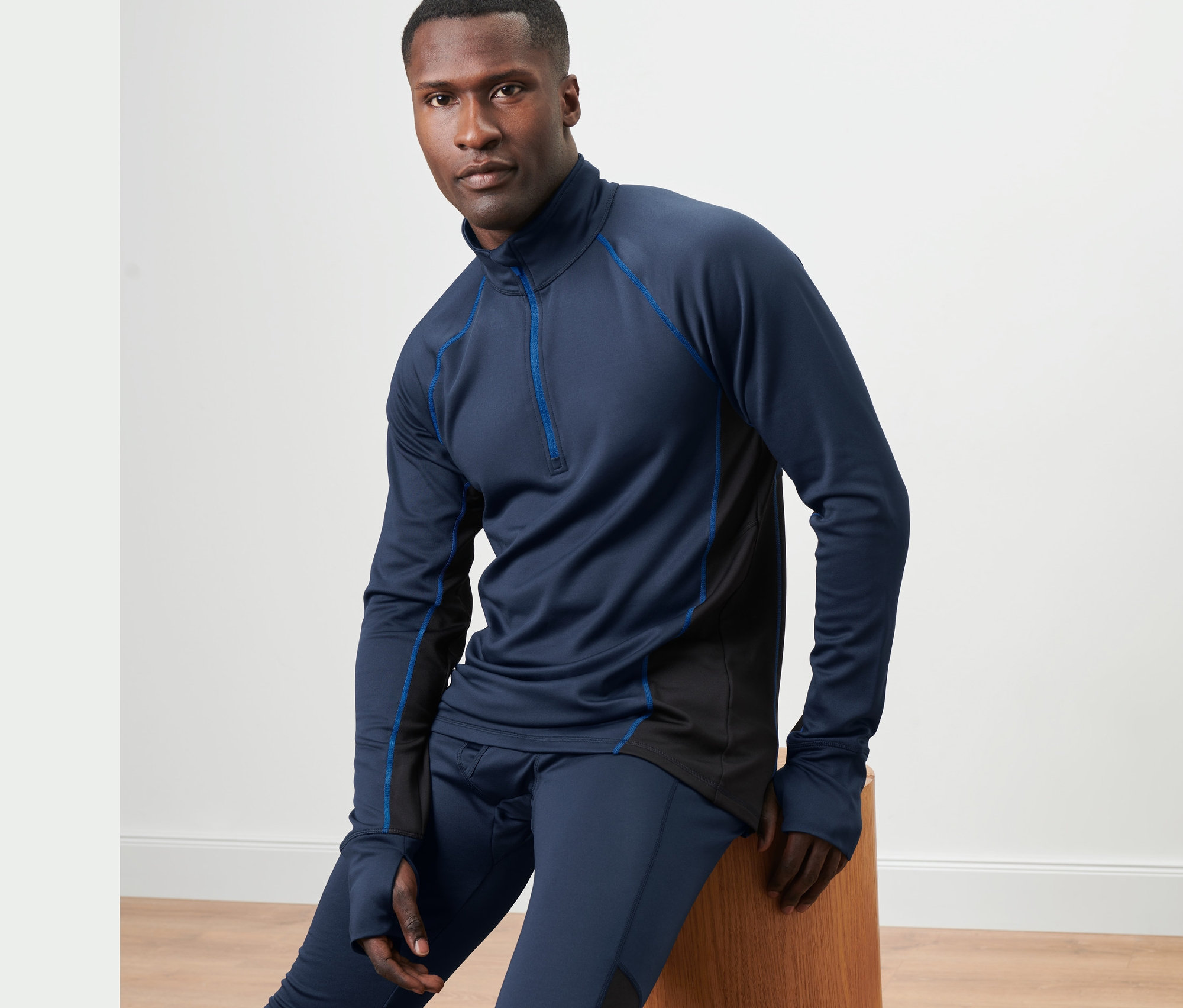 Un homme est assis sur un tabouret en bois et porte un t-shirt fonctionnel thermique bleu à manches longues.