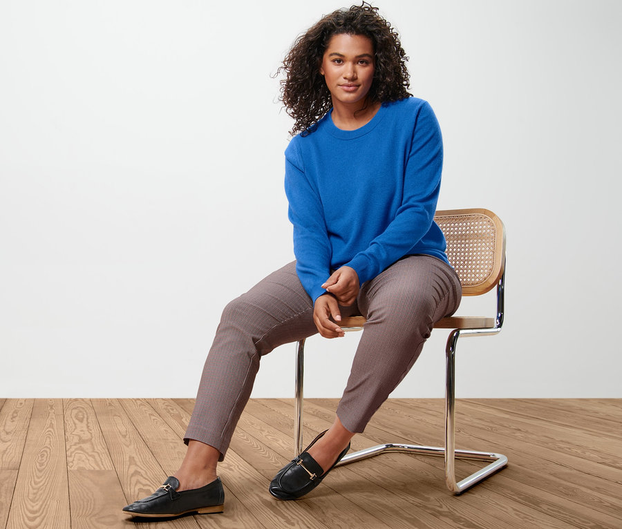 Une femme est assise sur une chaise et porte un pull en maille fine avec du cachemire, bleu cobalt et un pantalon stretch à carreaux.