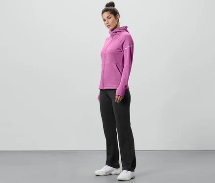 Femme debout de profil portant un sweat à capuche rose et un pantalon thermique noir.