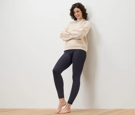 Une femme se tient les bras croisés contre un mur et porte un legging doublé.