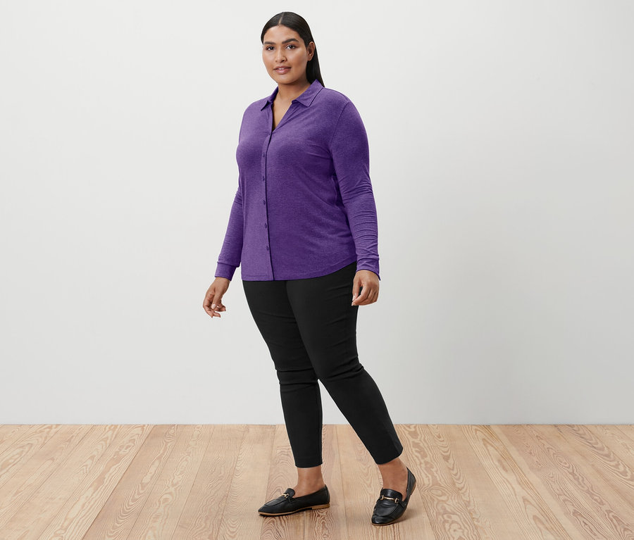 Femme marchant portant une blouse violette avec patte de boutonnage, un pantalon noir et des mocassins noirs.