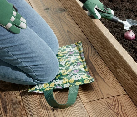 Femme agenouillée sur un coussin pour genoux, plantant des oignons dans la terre.