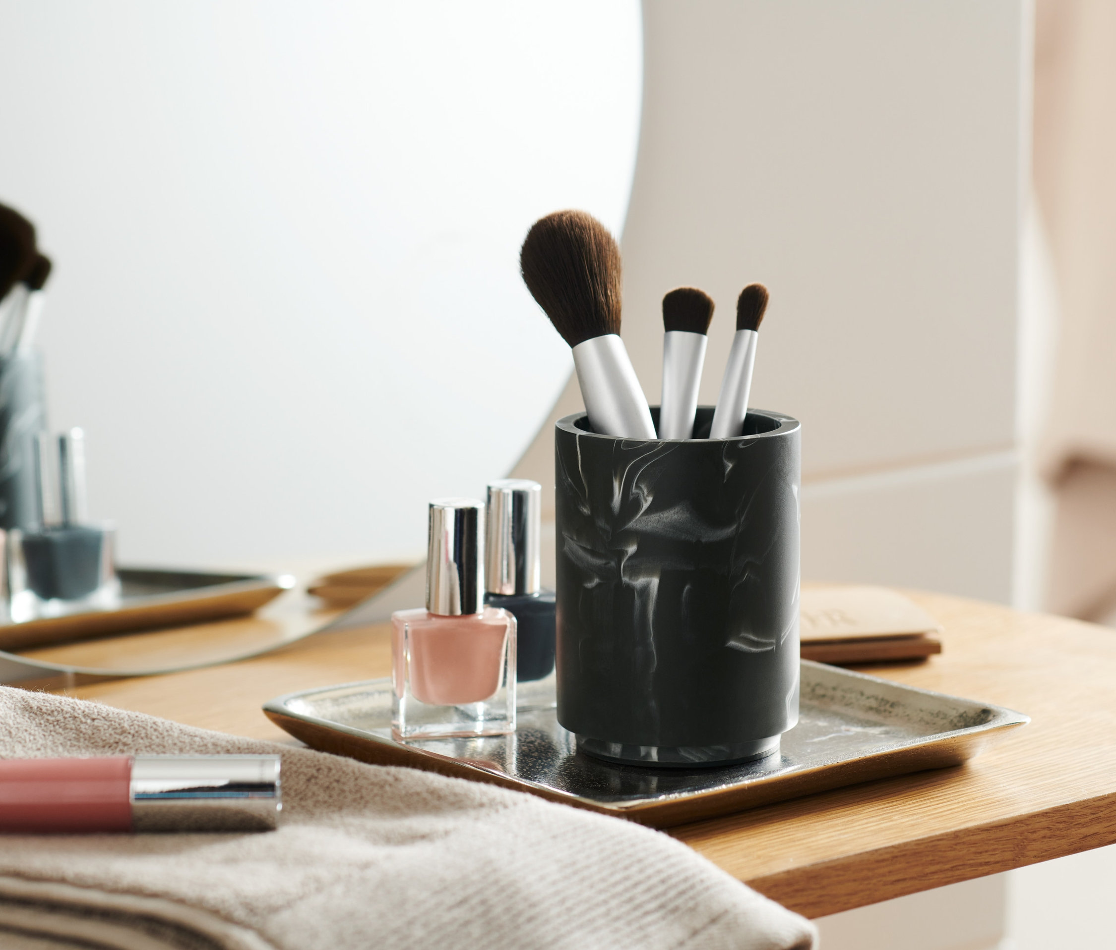 Pinceaux de maquillage dans un pot finition marbrée à côté de vernis à ongles sur un plateau.