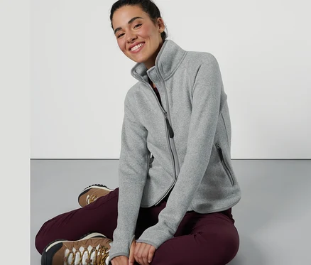 Une femme est assise et porte une veste en maille polaire gris-clair.