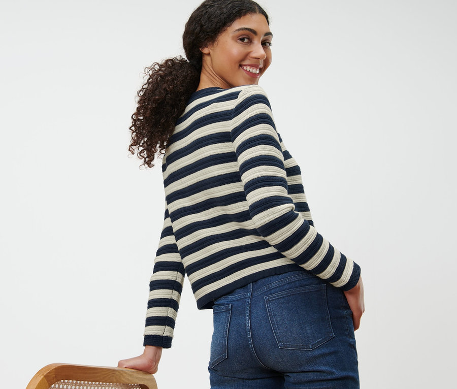 Une femme souriante regarde par-dessus son épaule et porte un cardigan en maille structurée et un jean.