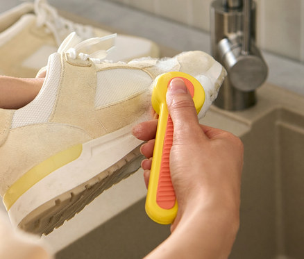 Une femme nettoie une chaussure avec une brosse à chaussures au-dessus d'un lavabo.