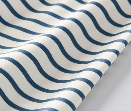 Gros plan sur un t-shirt pour enfant avec indice de protection UV 80, rayé de vagues bleues sur fond blanc.