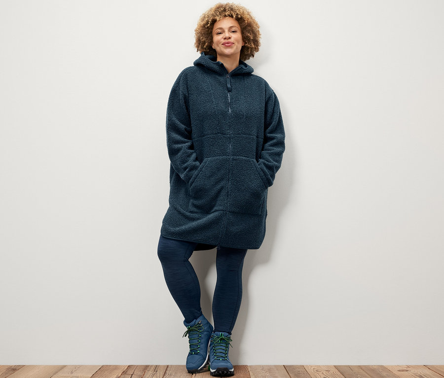 Femme posant en legging de sport et manteau en teddy oversize.