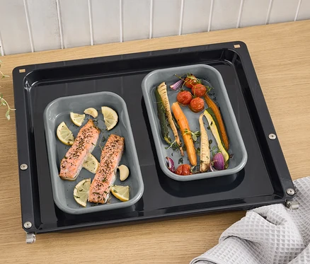 Deux brasiers en émail gris avec saumon, citron et légumes sur une plaque de cuisson.