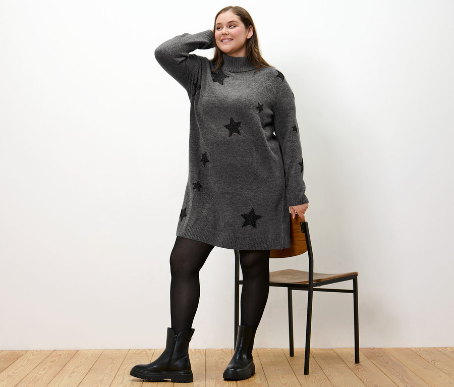 Femme posant en robe en maille à col roulé avec des étoiles noires, portant des bottes et des collants noirs.